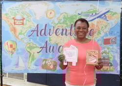 Smiling woman holding gift package in front of banner showing a map of the world. Smiling woman holding gift package in front of banner showing a map of the world.