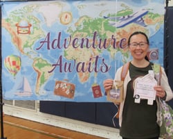 Smiling woman holding gift package in front of banner showing a map of the world. Smiling woman holding gift package in front of banner showing a map of the world.
