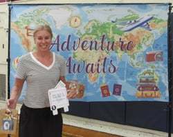 Smiling woman holding gift package in front of banner showing a map of the world.