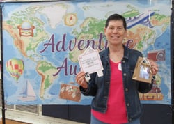 Smiling woman holding gift package in front of banner showing a map of the world. Smiling woman holding gift package in front of banner showing a map of the world.