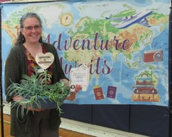 Smiling woman holding gift package in front of banner showing a map of the world.